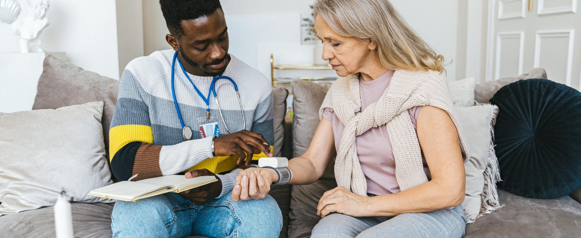 Healthcare professional checking blood pressure of elderly woman in a cozy indoor setting.