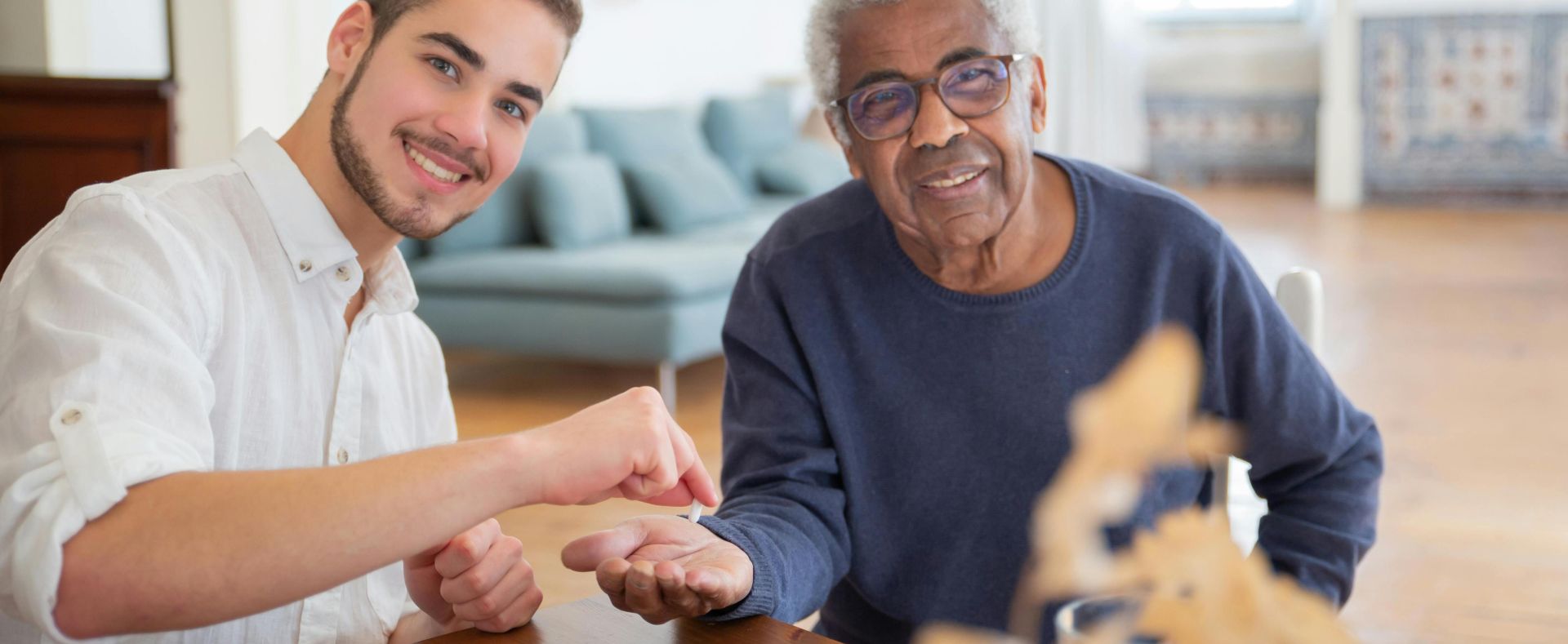 Smiling young man and senior man bonding indoors at a wooden table.
