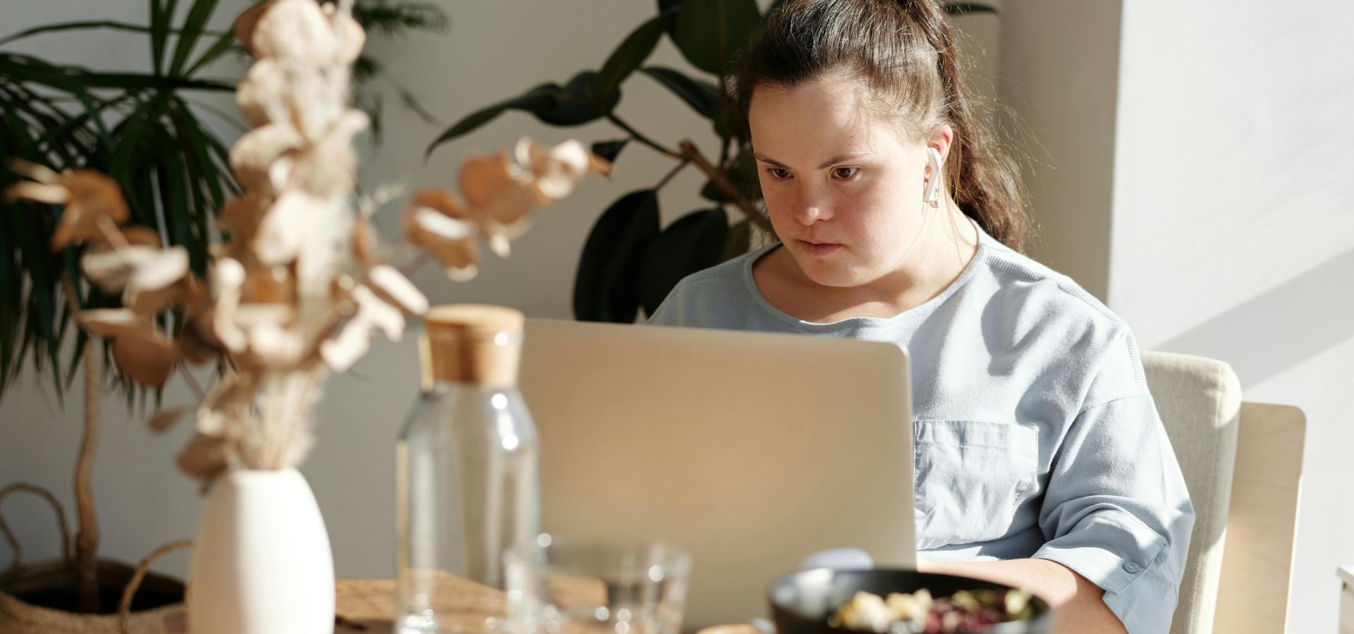 Young woman with Down syndrome using a laptop at a cozy home setting, enjoying leisure time.